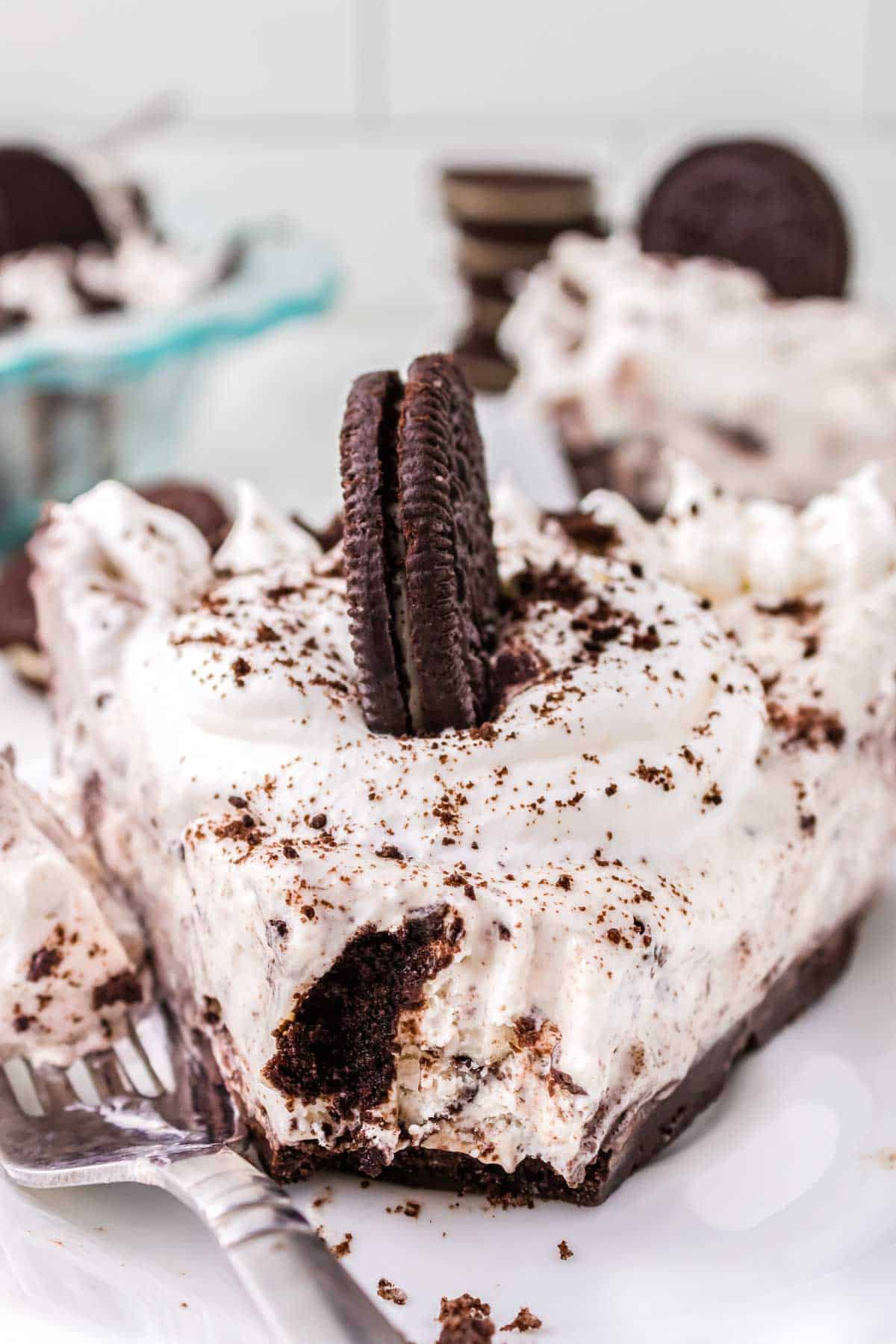 A slice of no-bake Oreo pie on a white plate with. a forkful taken out of it.