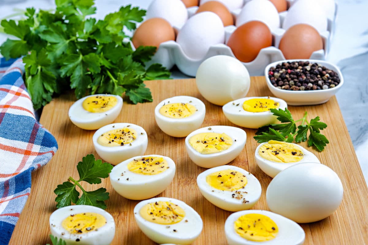 a cutting board with sliced hard boiled eggs and unpeeled hard boiled eggs in the background