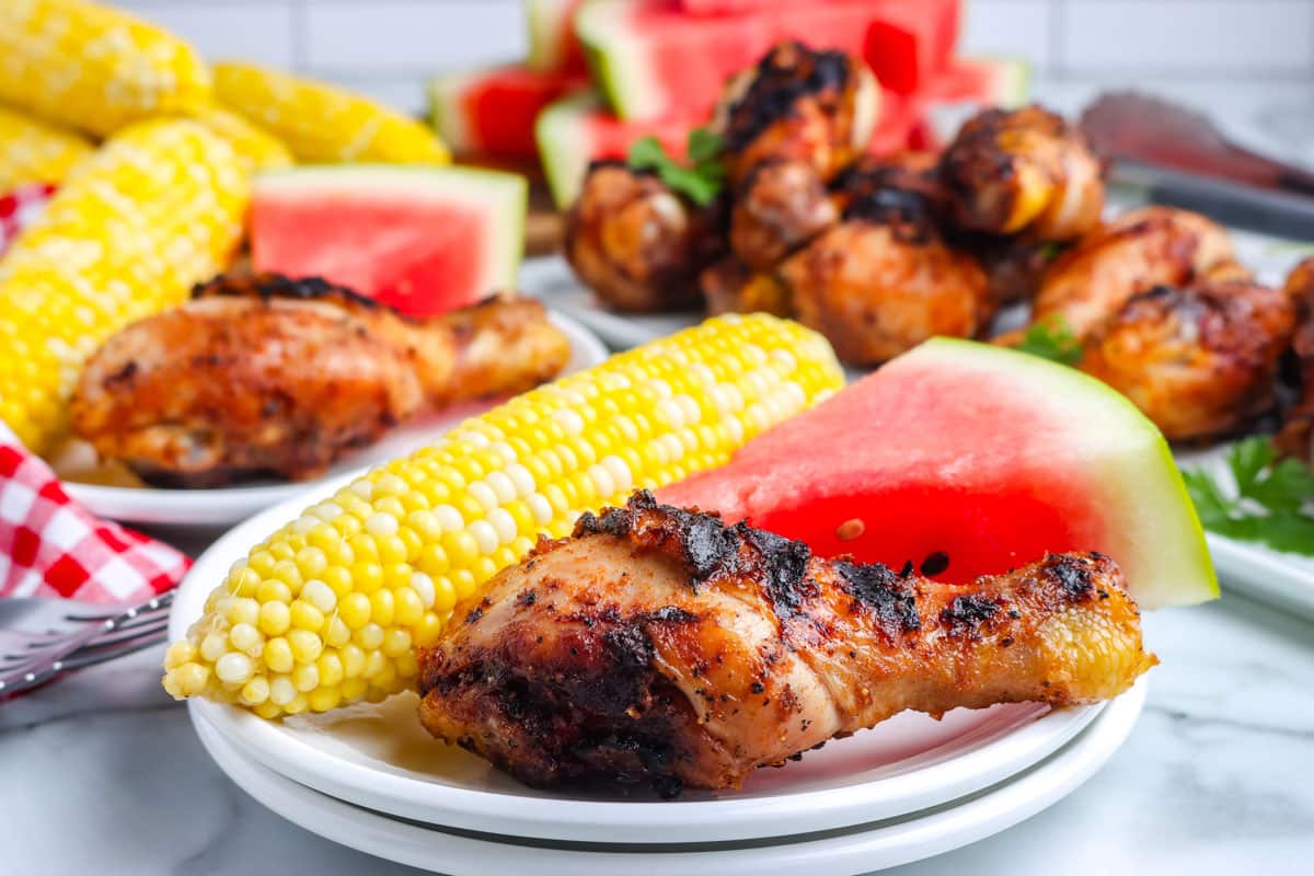 Chicken, corn, and watermelon on a white plate.