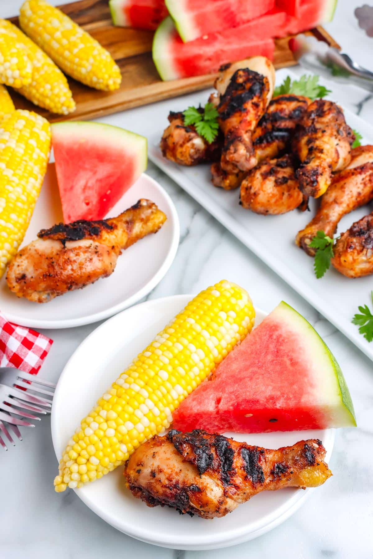 Chicken drumsticks on plates with corn and watermelon.