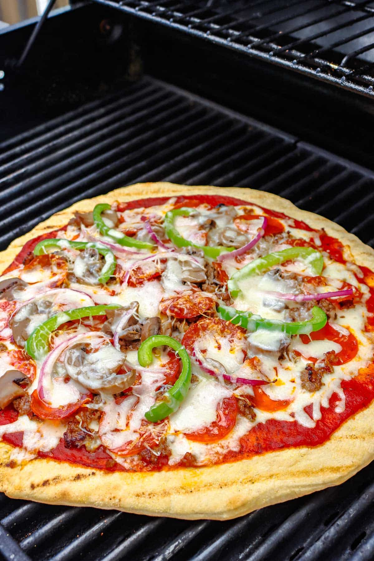 The finished grilled pizza on a grill.