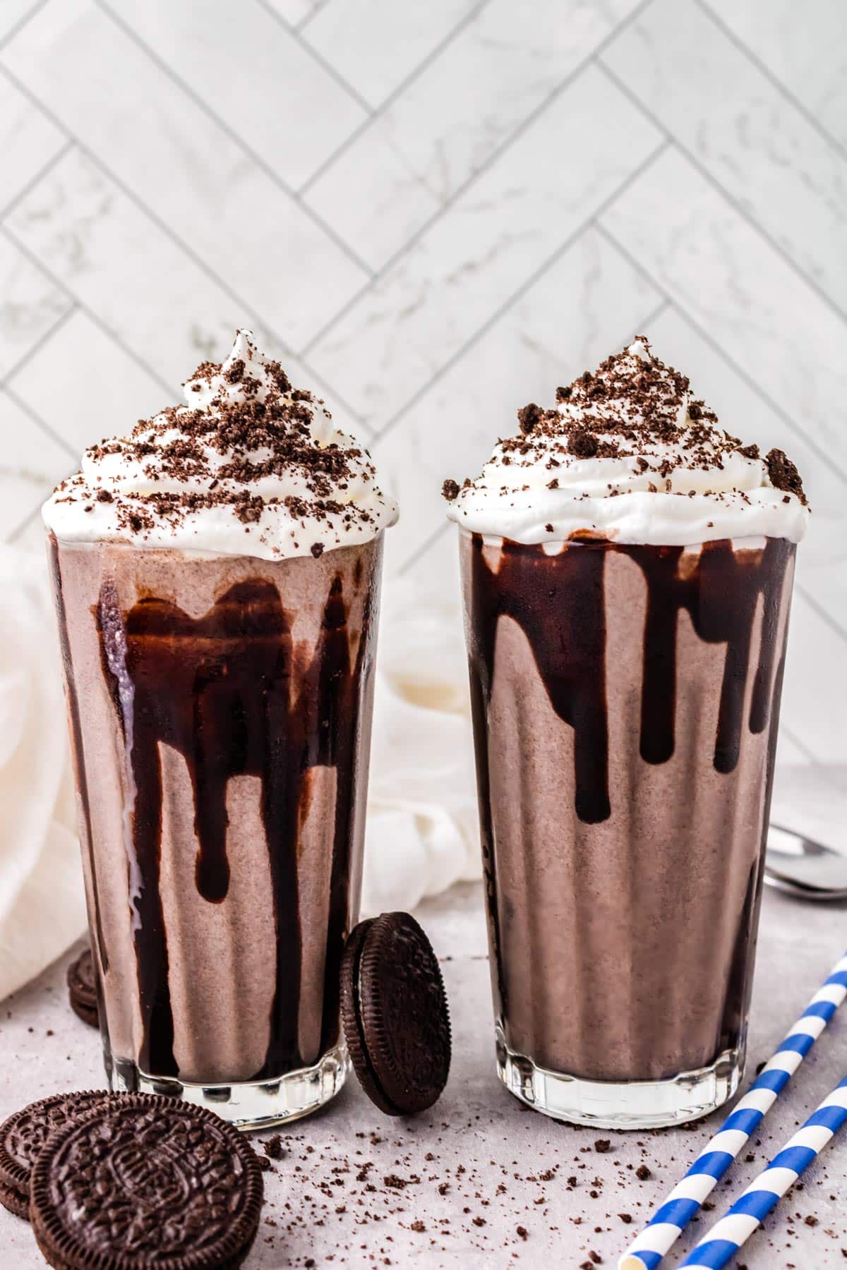 Oreo Milkshakes in clear glasses and garnighed with chocolate syrup, whipped cream, and Oreo crumbs.