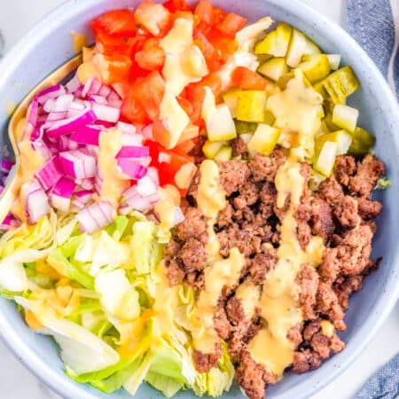 A bowl made with ground beef, lettuce, red nion, tomatoes, pickles, and a burger sauce.