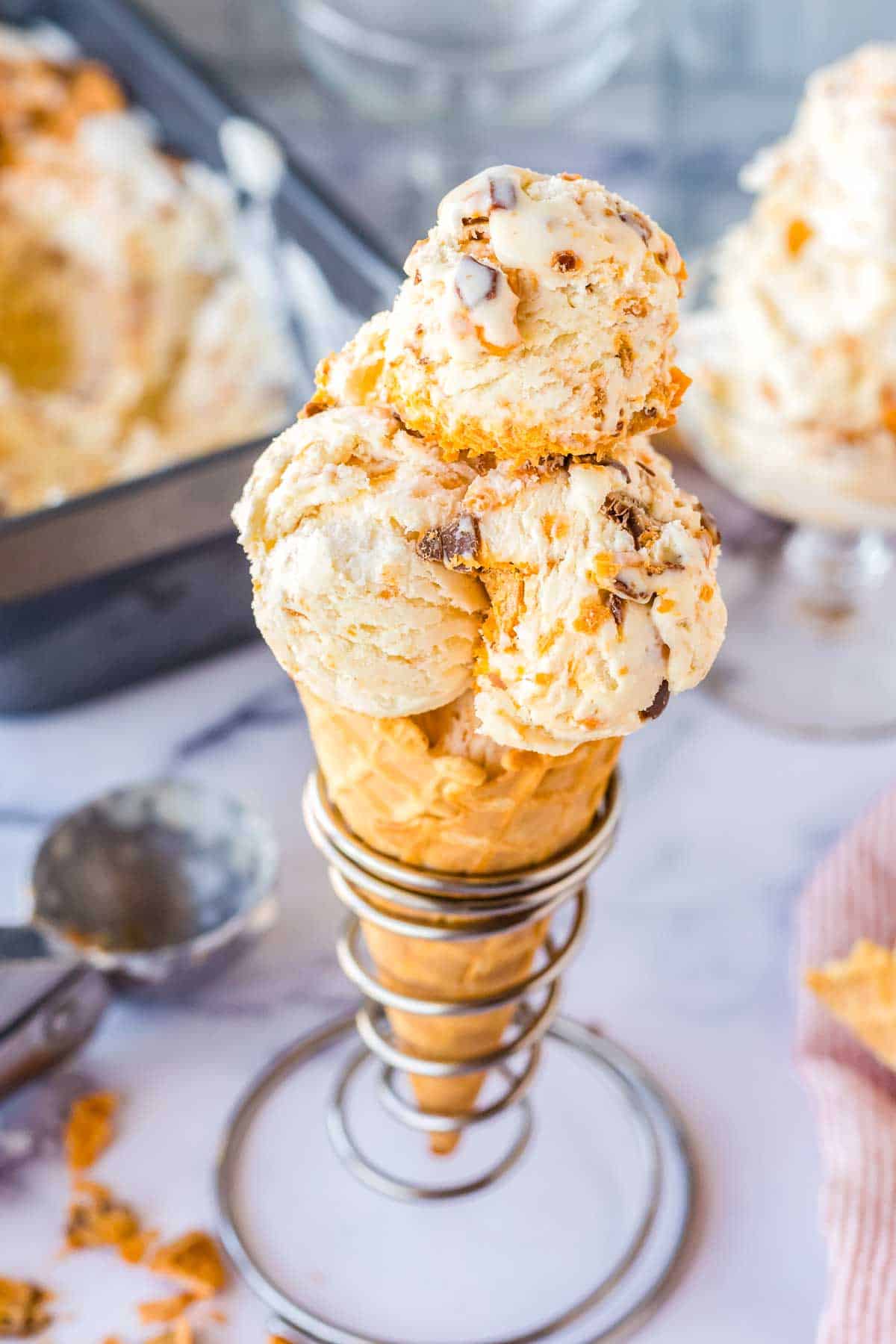 Three scoops of Homemade Butterfinger ice cream on a waffle cone.