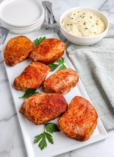 Six baked boneless pork chops on a white serving platter.