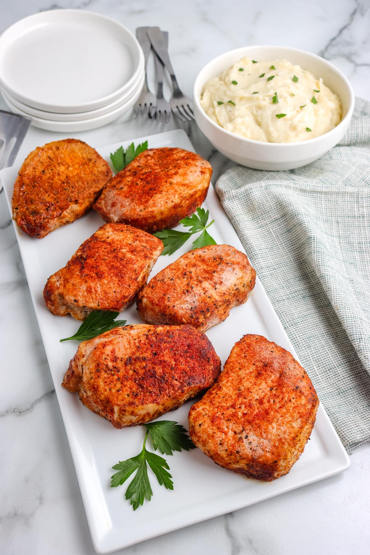 Six baked boneless pork chops on a white serving platter. 