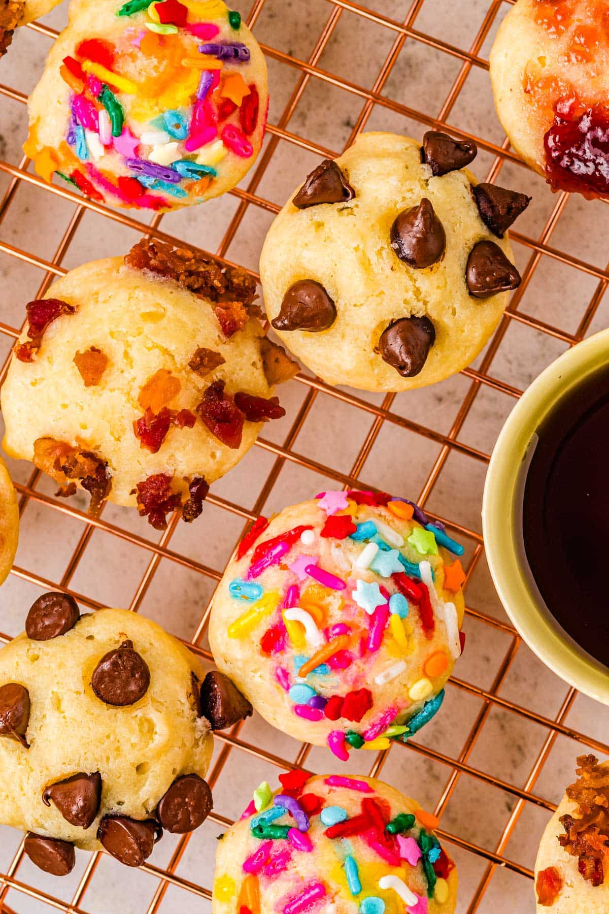 Pancake bits with various toppings like bacon, chocolate chips, jam, and cereal on a wire rack. 