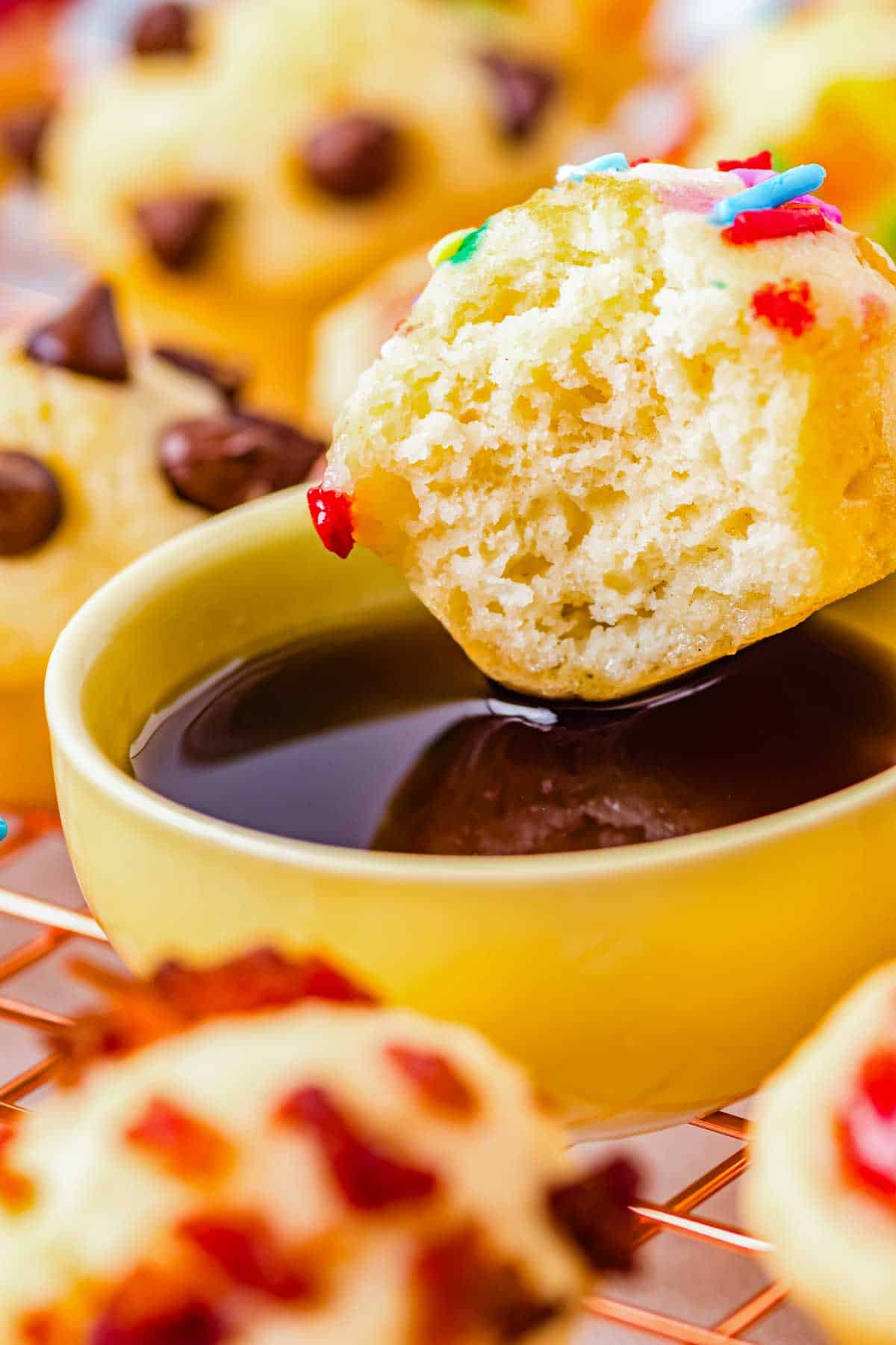 A mini pancake bite with a bite taken out of it dipped into syrup.