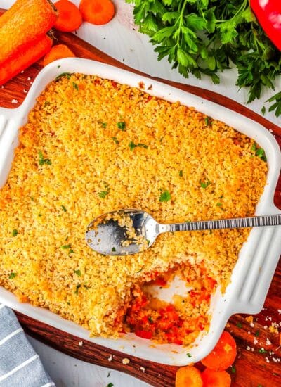The finished carrot casserole in a baking dish with a serving spoon resting on the top.