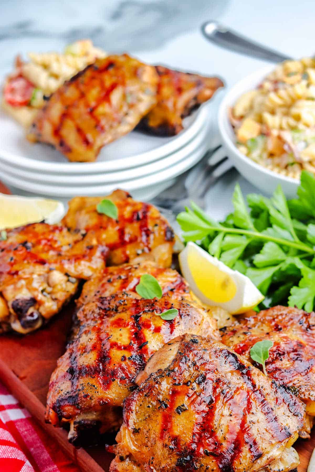 a platter of grilled chicken thighs with some pasta salad and a plate of chicken thighs in the background
