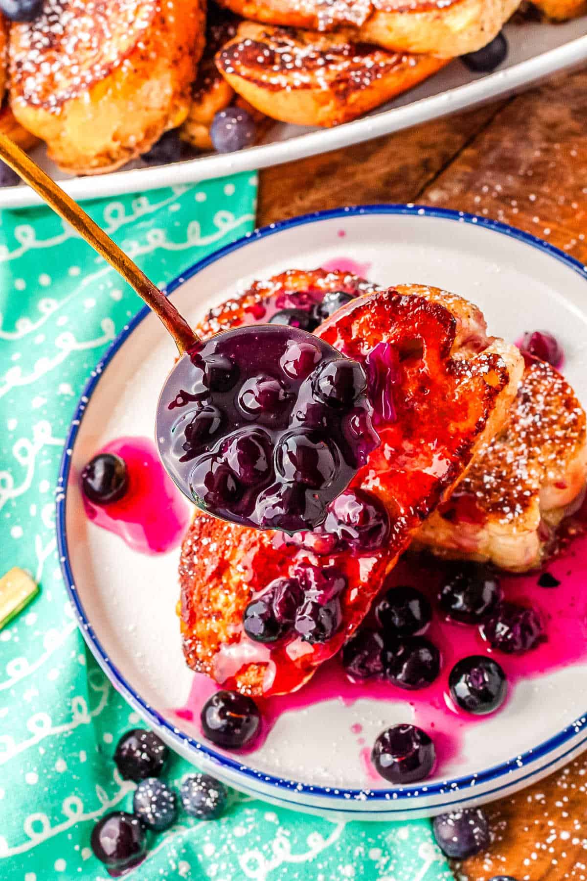 a ladle of blueberry syrup being poured over a plate of French toast