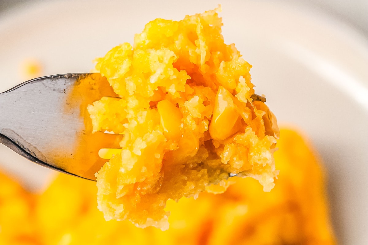 a fork taking a bite of corn casserole from a serving of the casserole on a plate