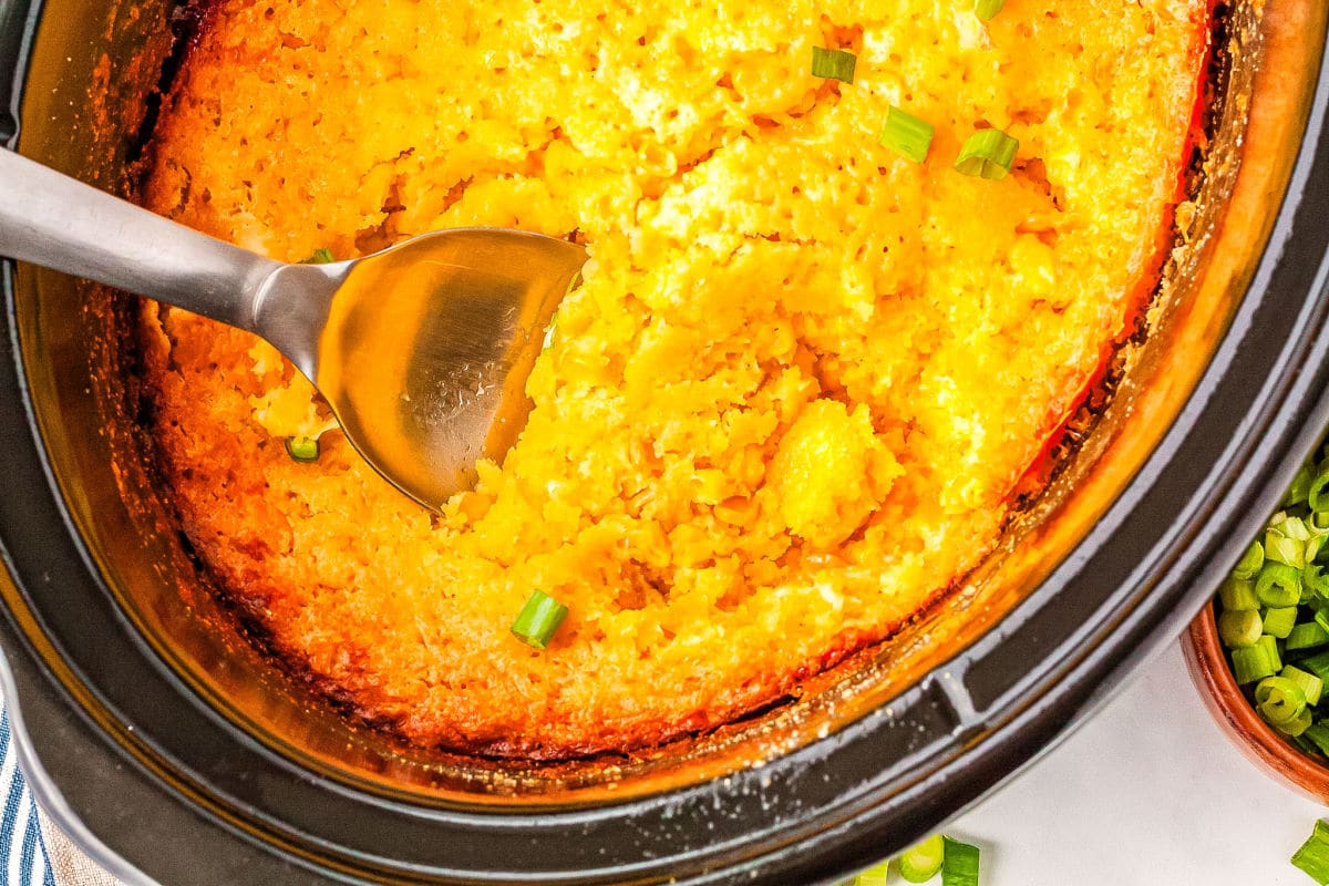 a spoon getting a scoop of corn casserole from a crockpot