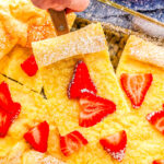 a baking dish with German pancakes with strawberries on it and one slice on a spatula