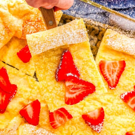 a baking dish with German pancakes with strawberries on it and one slice on a spatula