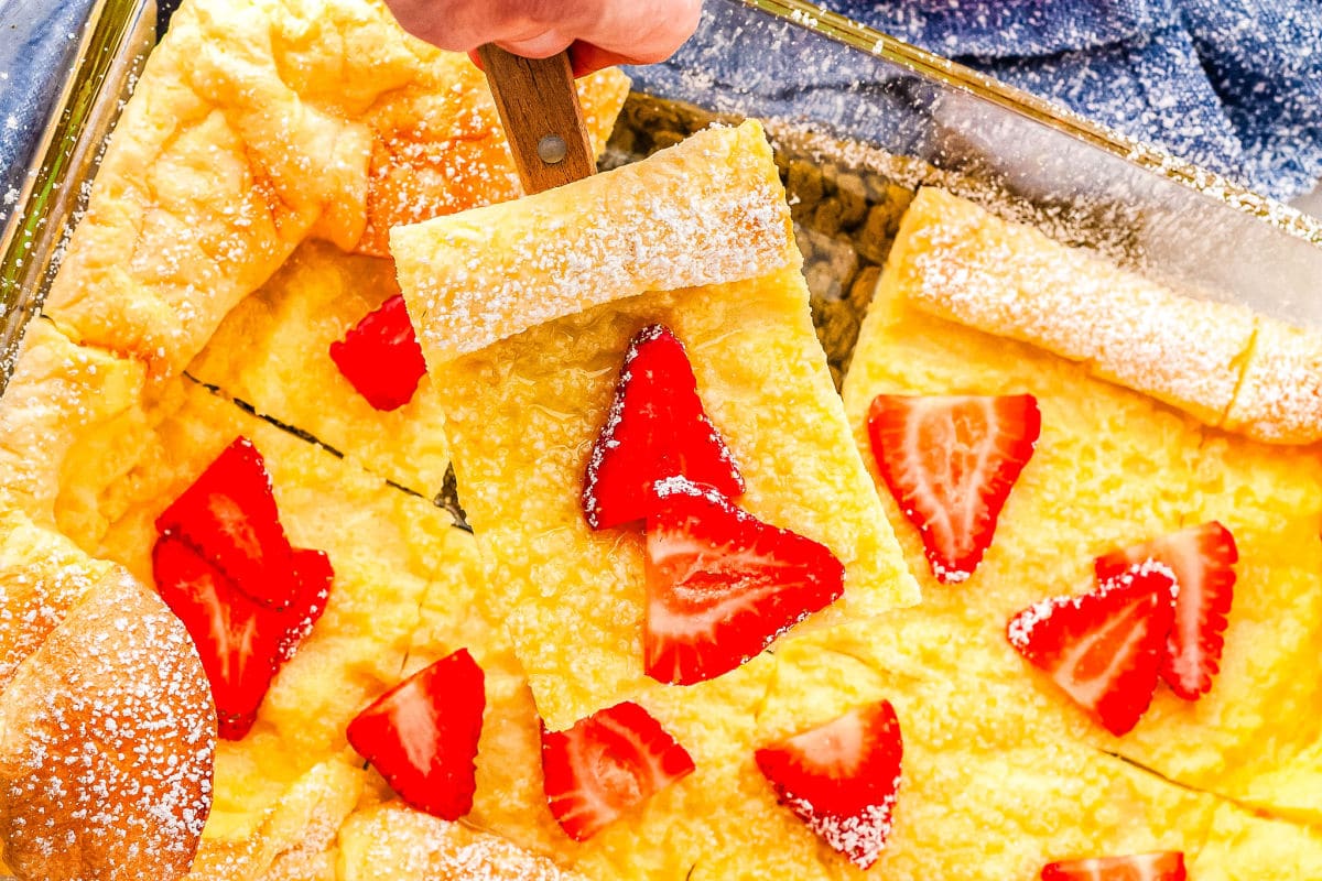 a baking dish with German pancakes with strawberries on it and one slice on a spatula