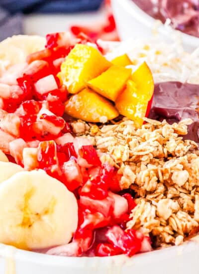 a bowl with acai and bananas, mangoes, strawberries, granola, and honey