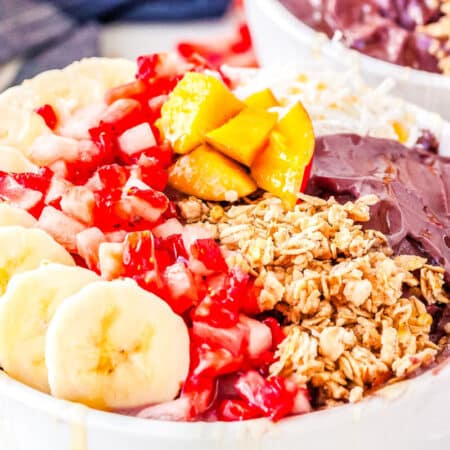a bowl with acai and bananas, mangoes, strawberries, granola, and honey
