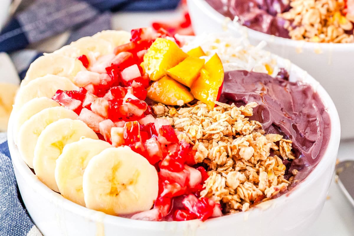 a bowl with acai and bananas, mangoes, strawberries, granola, and honey