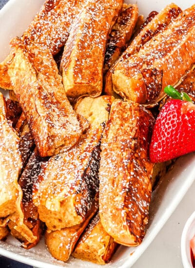 a plate of french toast sticks with strawberry and orange slices in the background