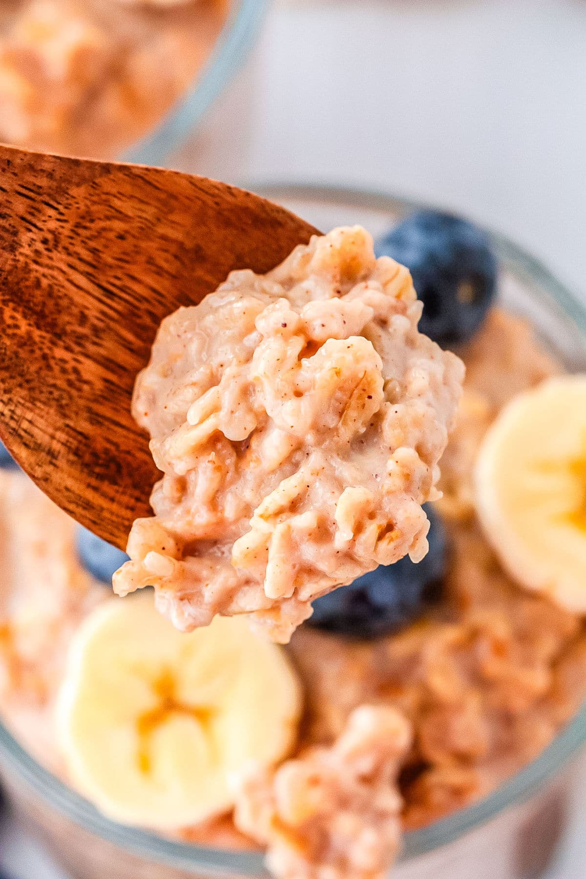 a close up of a spoonful of oatmeal breakfast cups with the rest of the fruit and oatmeal in the parfait glass behind