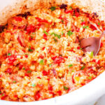 a crockpot full of sausage and rice casserole with a spoon taking a scoop out of it