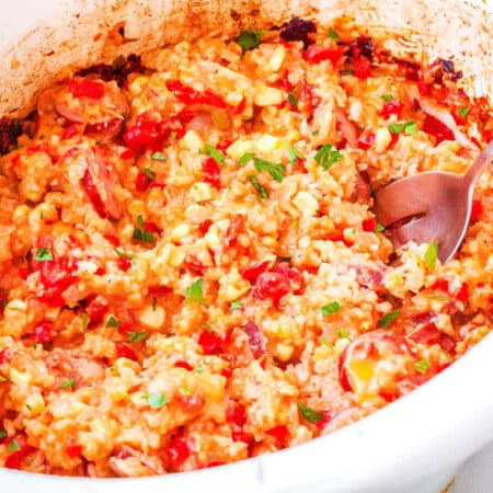 a crockpot full of sausage and rice casserole with a spoon taking a scoop out of it
