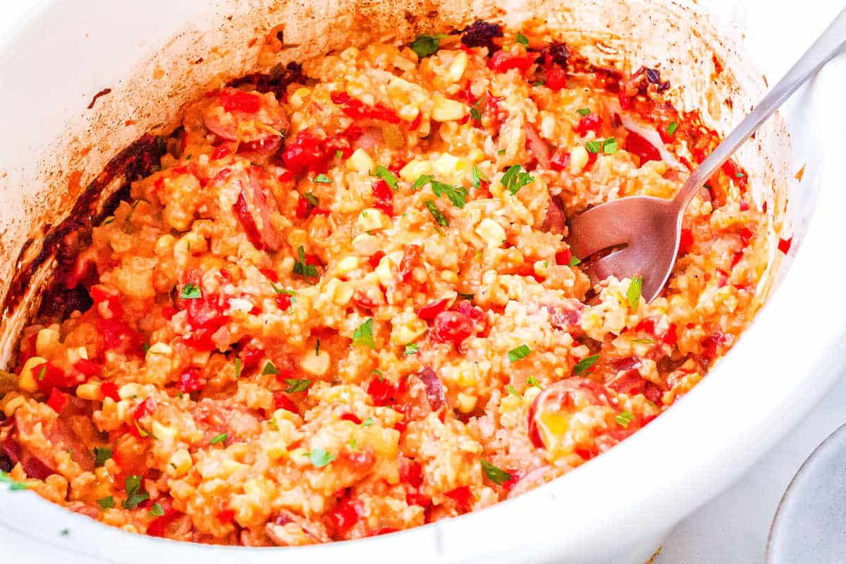 a crockpot full of sausage and rice casserole with a spoon taking a scoop out of it