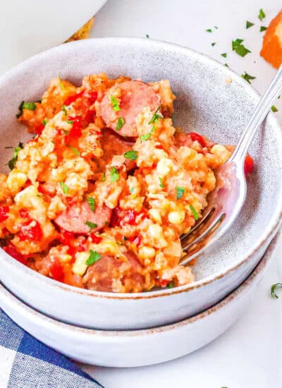 a bowl of sausage and rice casserole with a slice of bread on the side and a bowl of chives