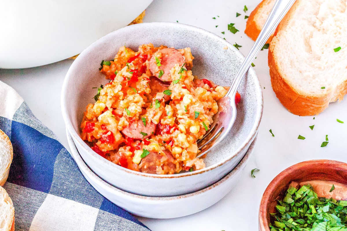 a bowl of sausage and rice casserole with a slice of bread on the side and a bowl of chives